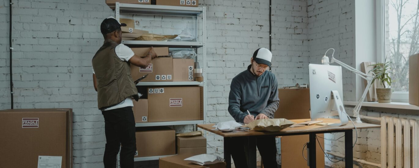 Two workers handling packages and organizing stock in a warehouse setting.