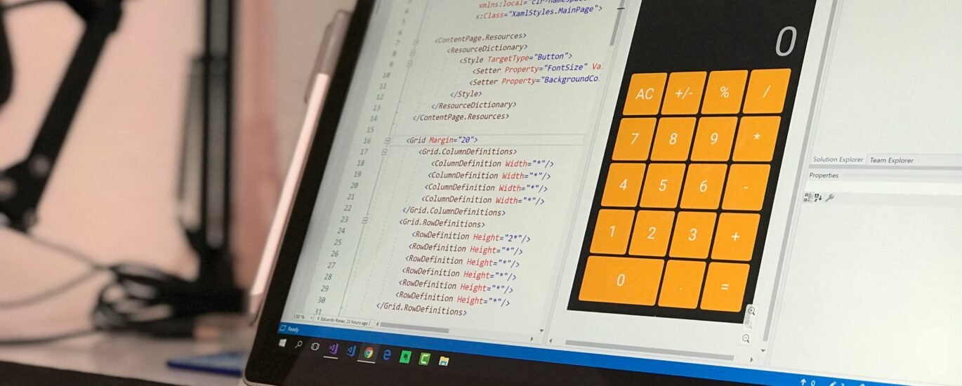 A laptop screen shows a coding application with a calculator design in a tech office setting.